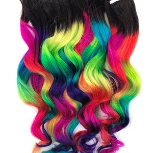 Wavy clip-in hair extensions with black roots blending into neon rainbow colors: pink, yellow, green, blue, and purple.
